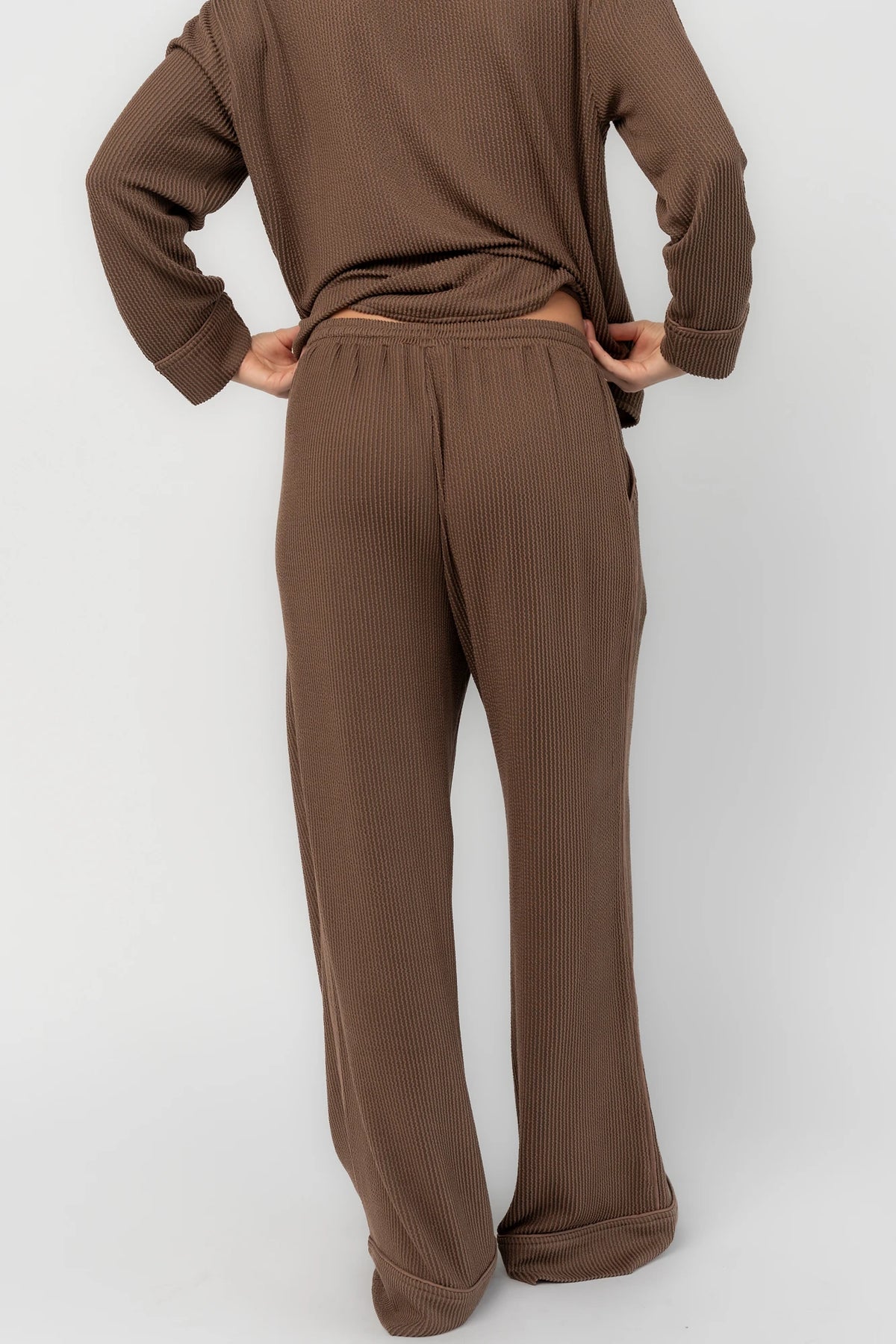 Brown ribbed pajama set with a button-front V-neck top, long sleeves, chest pocket, and wide-leg pants with an elastic drawstring waist.