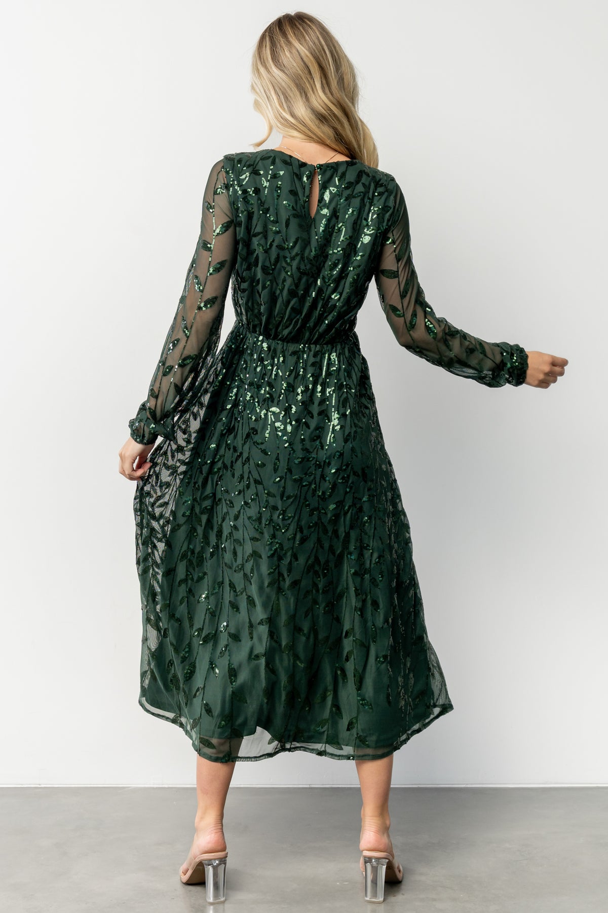 Detail shot of long sheer sleeve and elastic cuff on emerald sequin midi dress, highlighting fabric drape and embellishment finish.