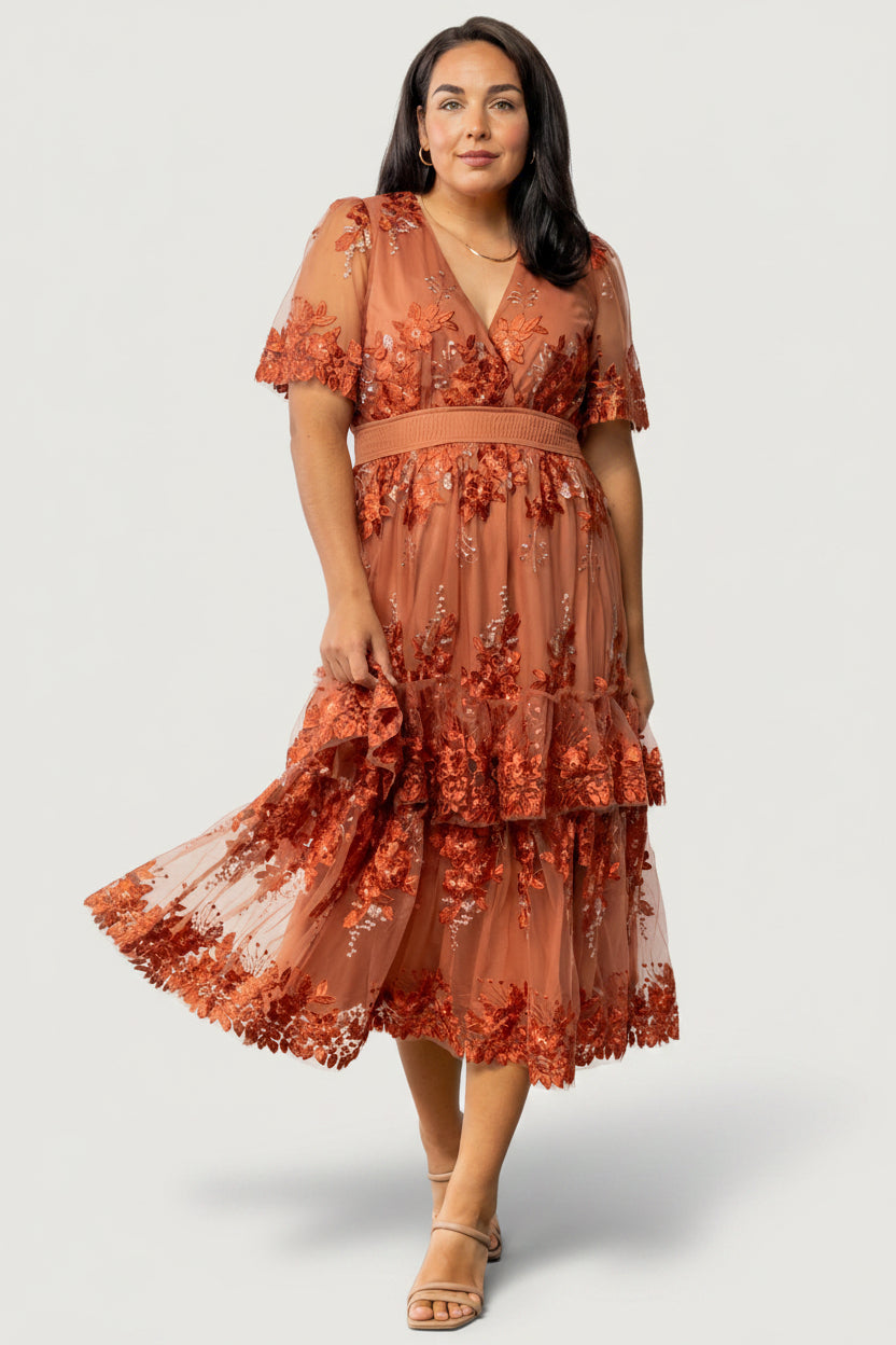 Three-quarter view of the Lotte rust midi dress on model highlighting tiered ruffle overlay and flow of embroidered tulle fabric.