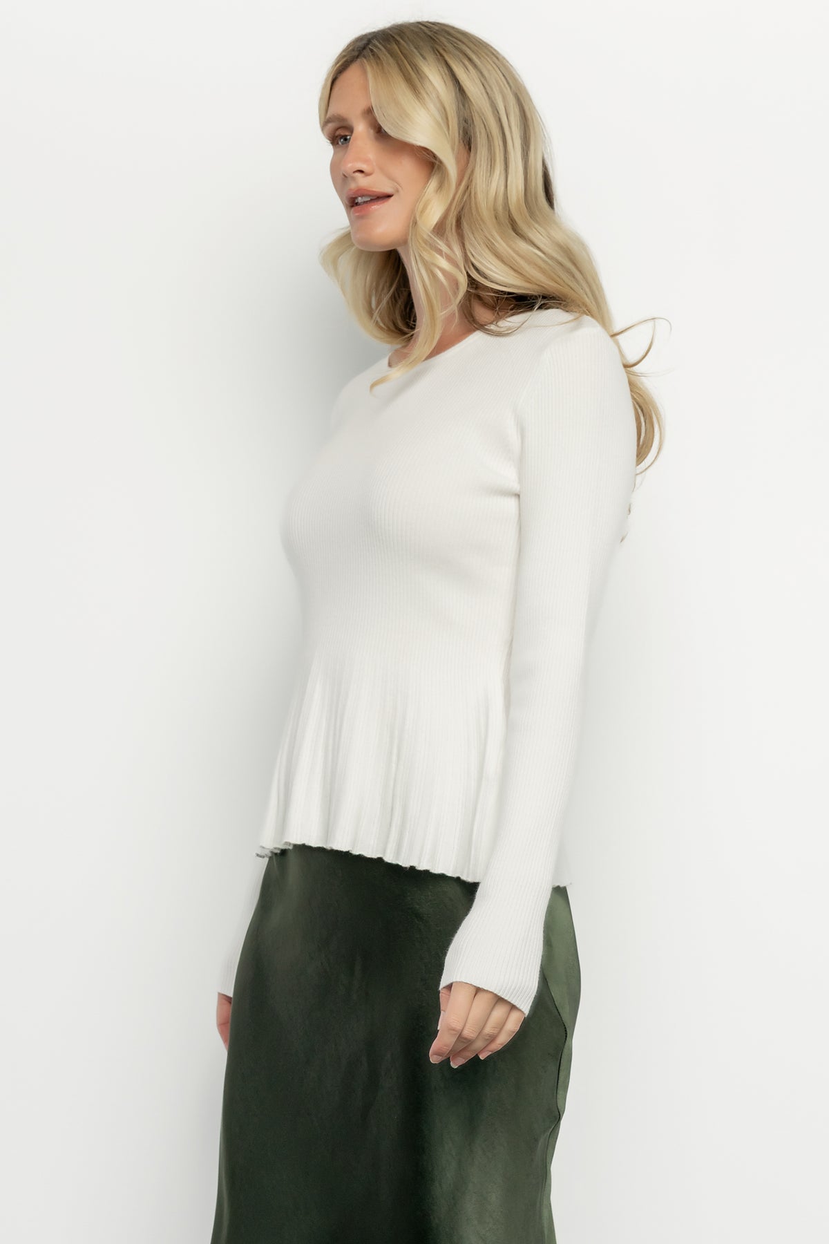 Full-length shot of model in Ainsley Ribbed Top showing fitted bodice, peplum waist detail, and raw hem with neutral accessories.