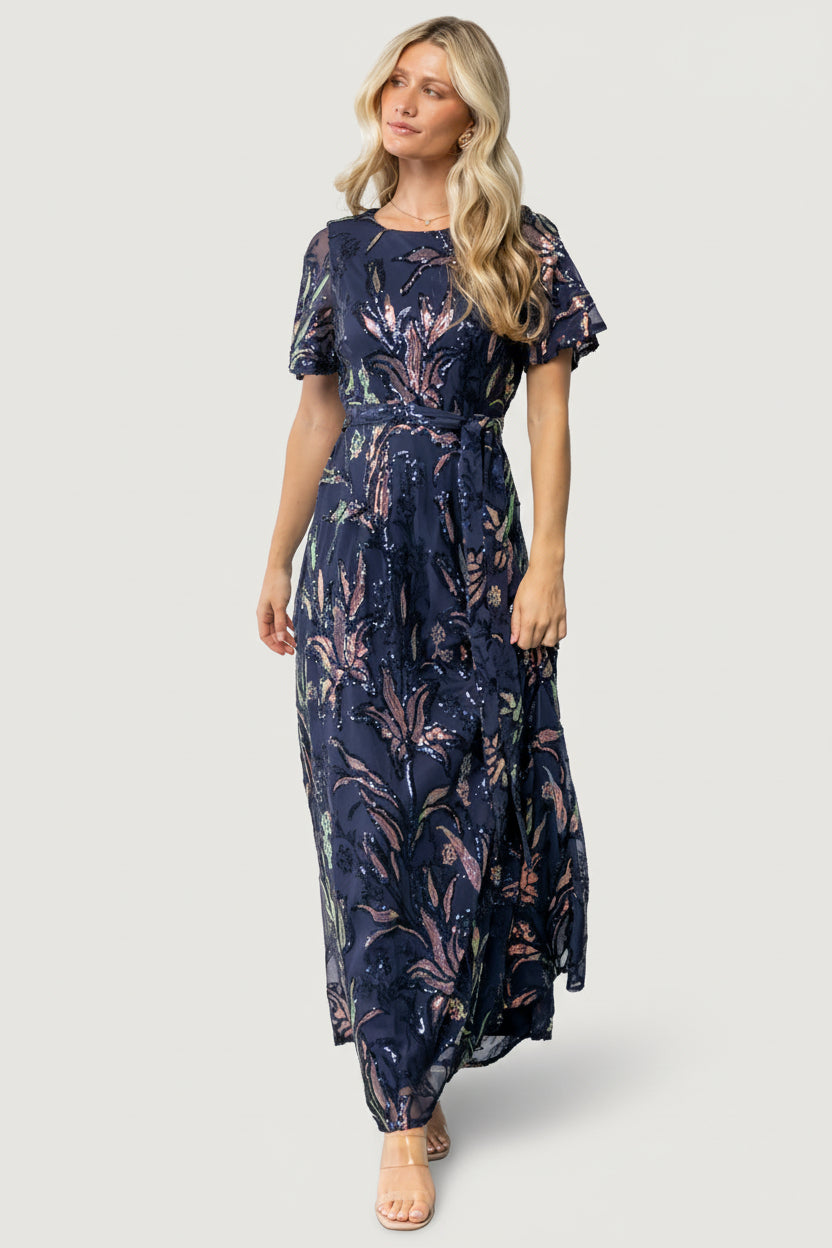 Front view of Muse Sequin Maxi Dress in dark blue multi, showing sequin leaf embellishment, round neckline, waist sash and flowing maxi skirt.
