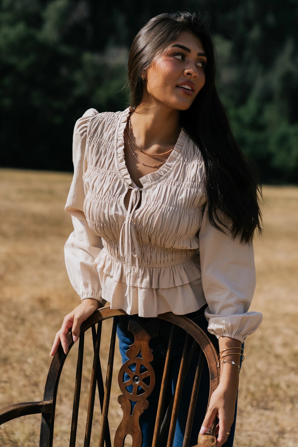 Marnie Smocked Top in Natural with smocked bodice, front bow ties, long sleeves, elastic cuffs, and peplum hem.