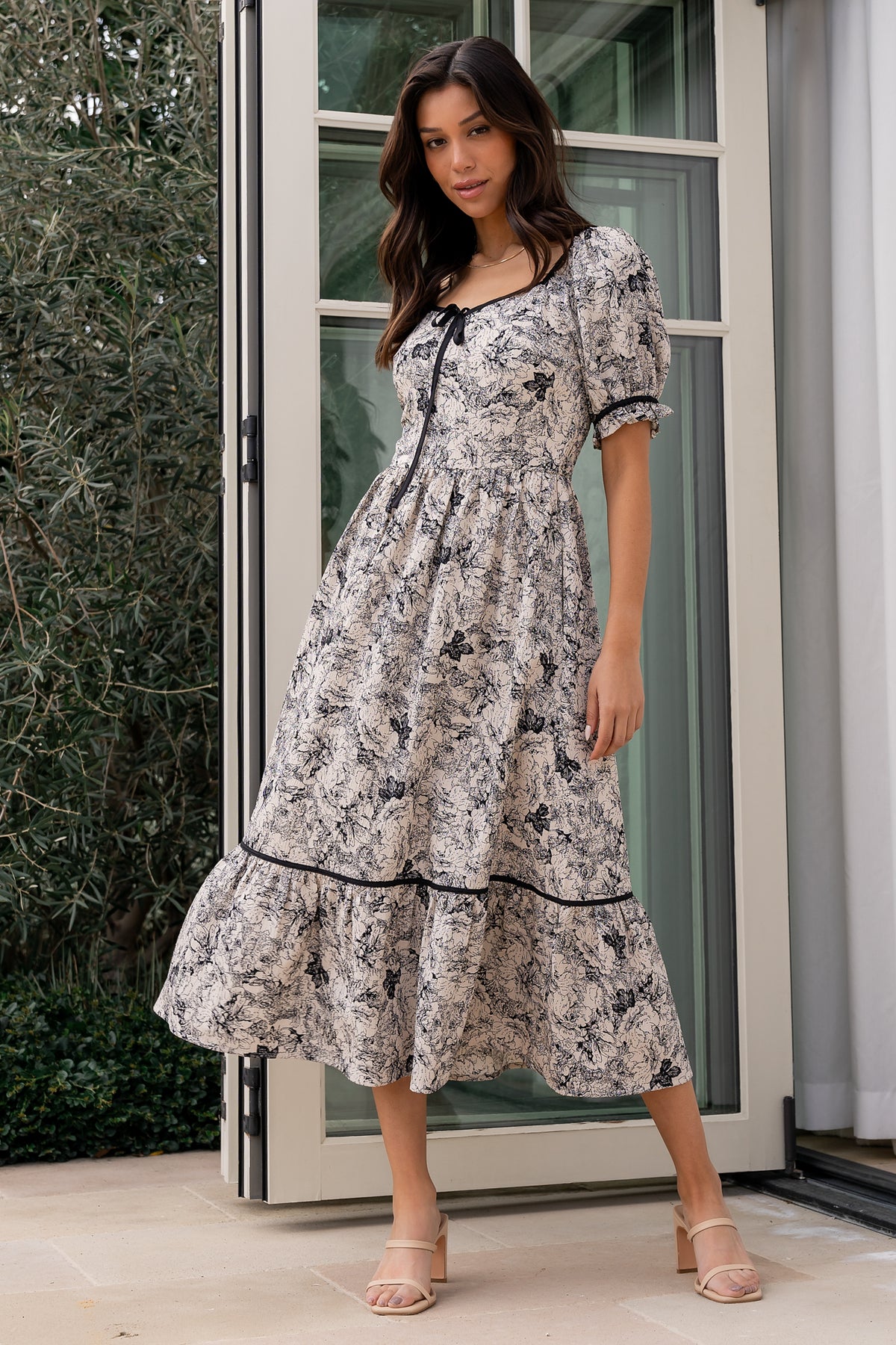 Close-up of textured cream and black floral fabric and decorative bow at neckline, highlighting fabric texture and trim details.