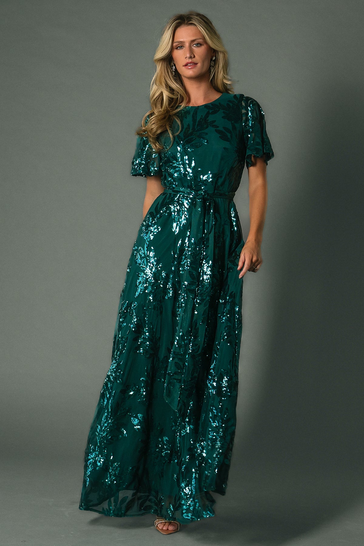Three-quarter view of Muse Sequin Maxi Dress in emerald, highlighting short sheer sleeves, round neckline, and sequin leaf pattern across bodice.
