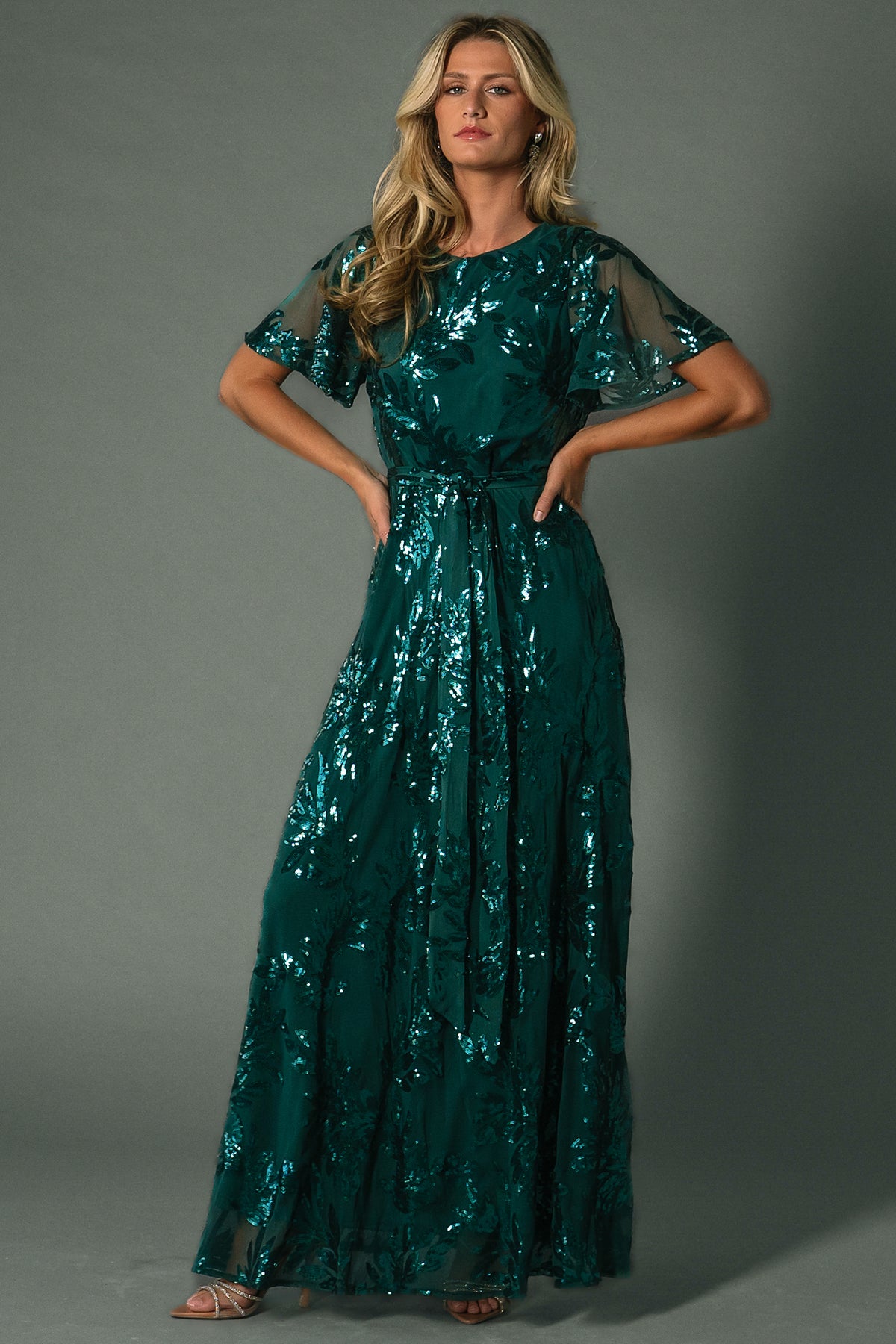 Model styling shot in Muse Sequin Maxi Dress emerald, paired with minimal accessories to emphasize sequin leaf pattern and evening wear silhouette.