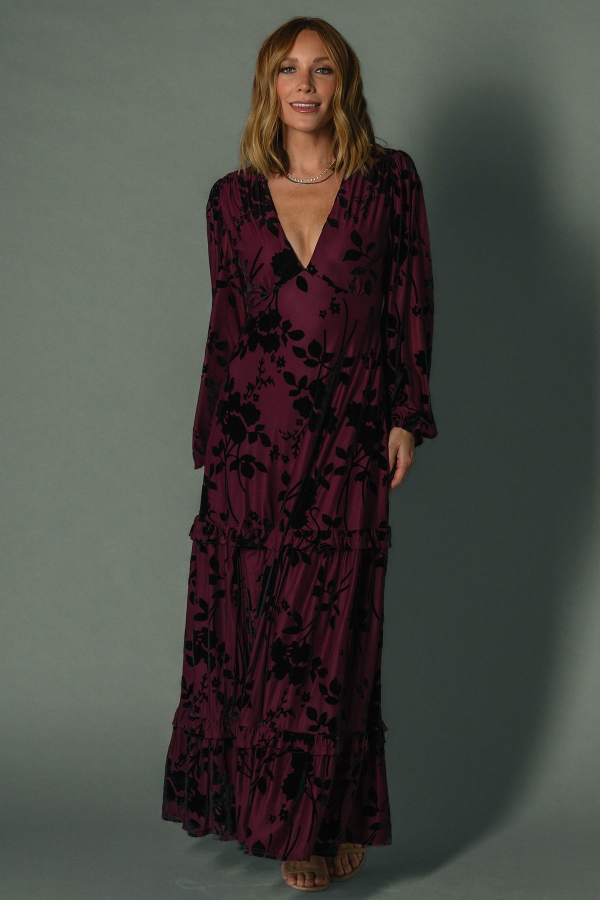 Model seated in mulberry velvet burnout maxi dress illustrating skirt movement, lined bodice, and unlined sleeves for comfort.