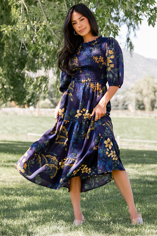Front view of Lena Tiered Midi Dress in navy with gold floral print on a model, showing smocked bodice, ruffle collar and tiered skirt in soft chiffon.