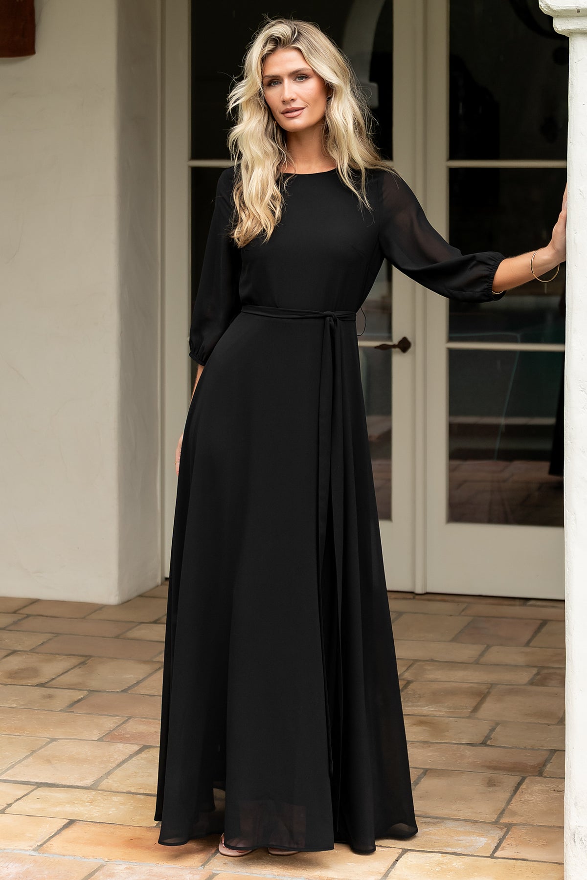 Full-length front view of Rebecca Maxi Dress in black on a model, showing rounded neckline, fitted back waist and flowing maxi skirt for elegant movement.
