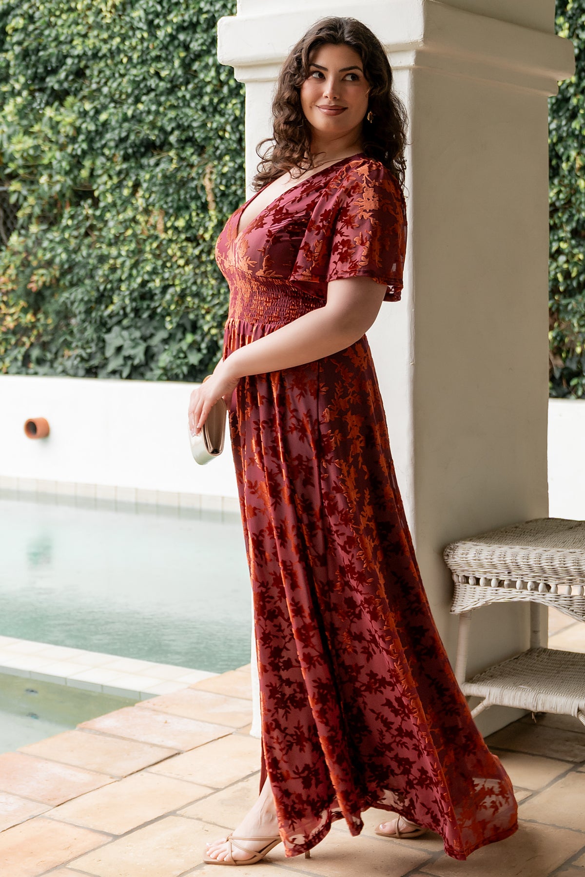 Model walking in Veronica velvet maxi dress rust, emphasizing left leg slit and elegant maxi length.