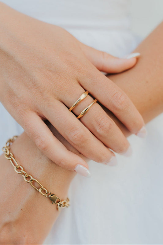 Close-up of Florence open-wave gold ring beside a bracelet on a neutral background, showing the ring's profile and polished finish.