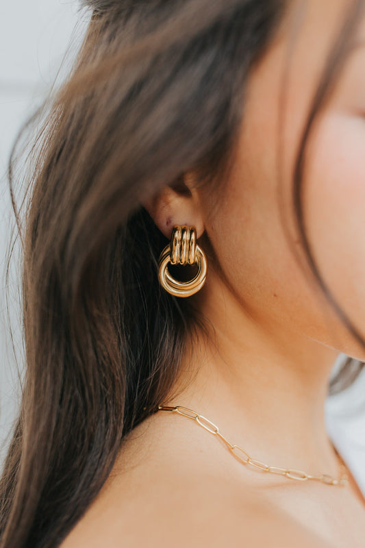Model wearing gold Hailey Earrings with Eloise necklace; close-up shows interlocking hoop silhouette, polished finish, and secure post-back closure.