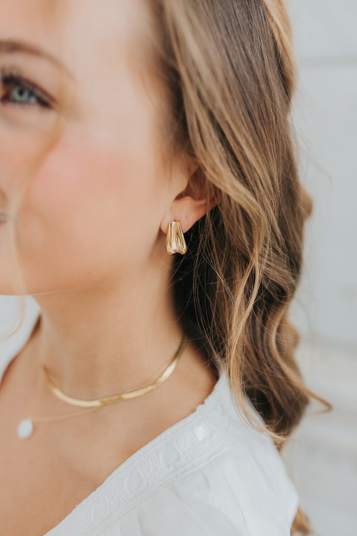 Close-up of The Sicily Hoop folded-metal gold hoop earring on white background, showing textured folded design and secure post-back closure.