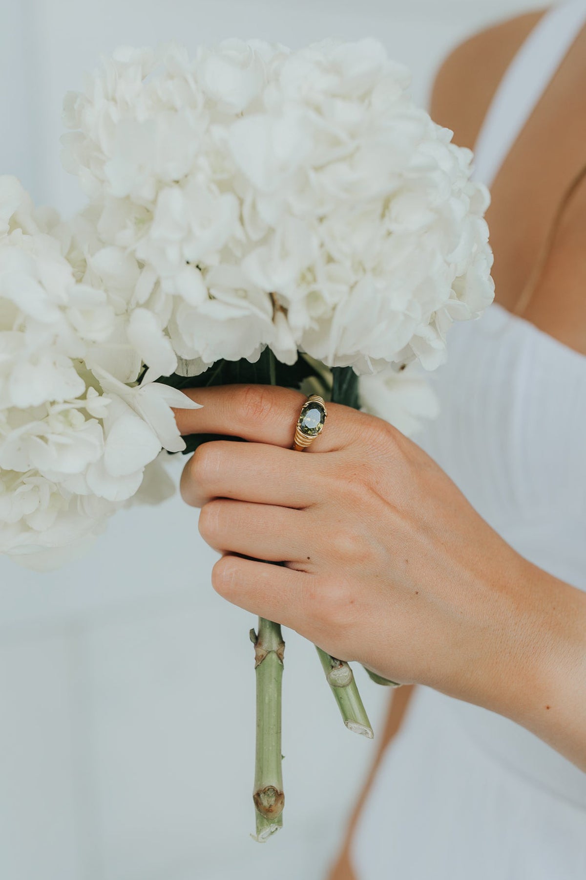 Flat lay of The Maddie ring on a neutral background showing the oval green stone and polished finish.