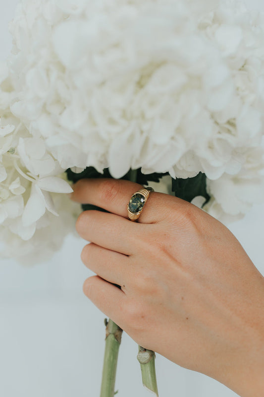 Front view of The Maddie emerald ring showing an oval green gemstone and polished ribbed 18K gold-plated band.