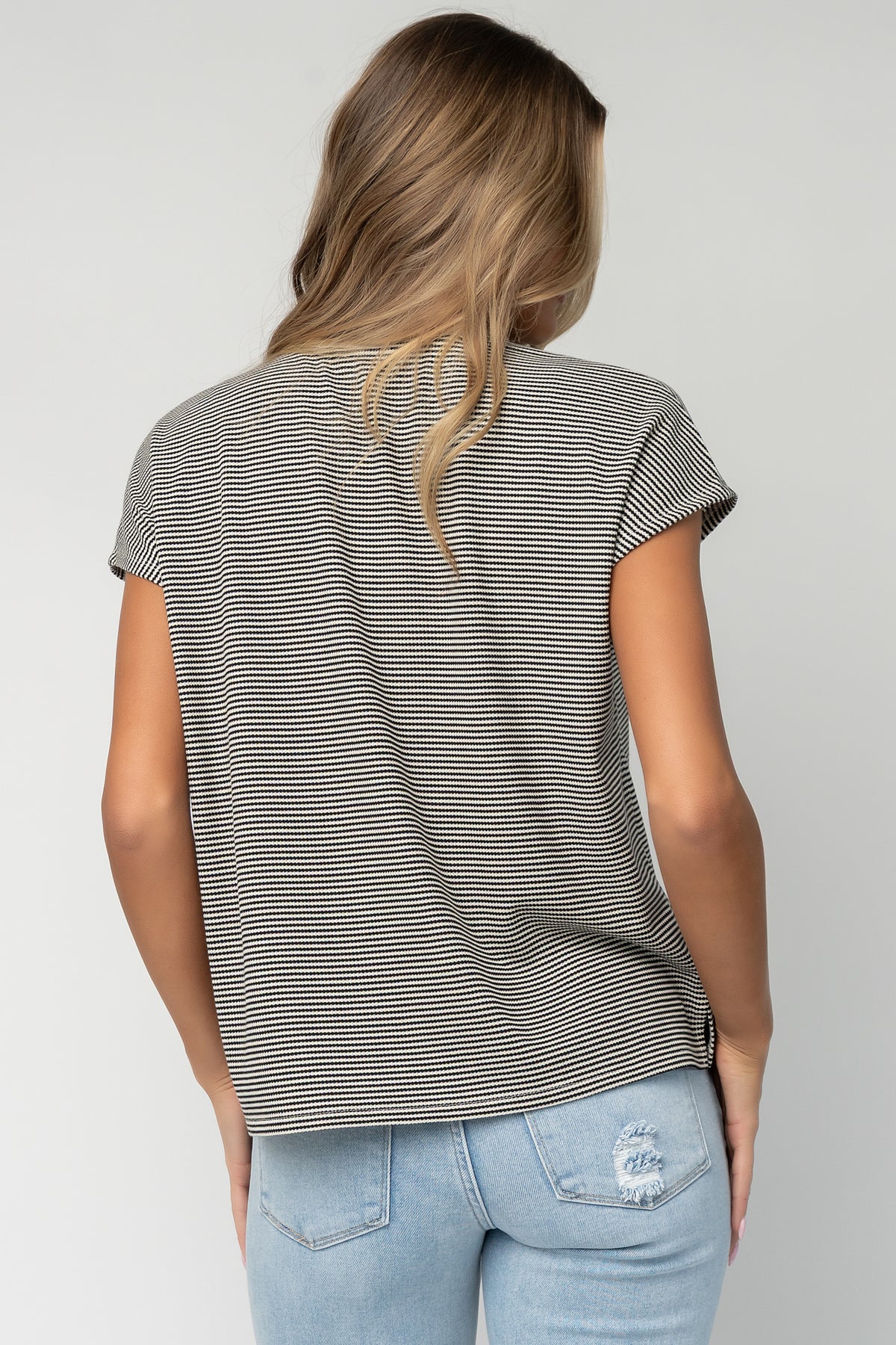 Model wearing Millie Striped Top in black and off-white with short sleeves and relaxed fit, styled with light-wash jeans.