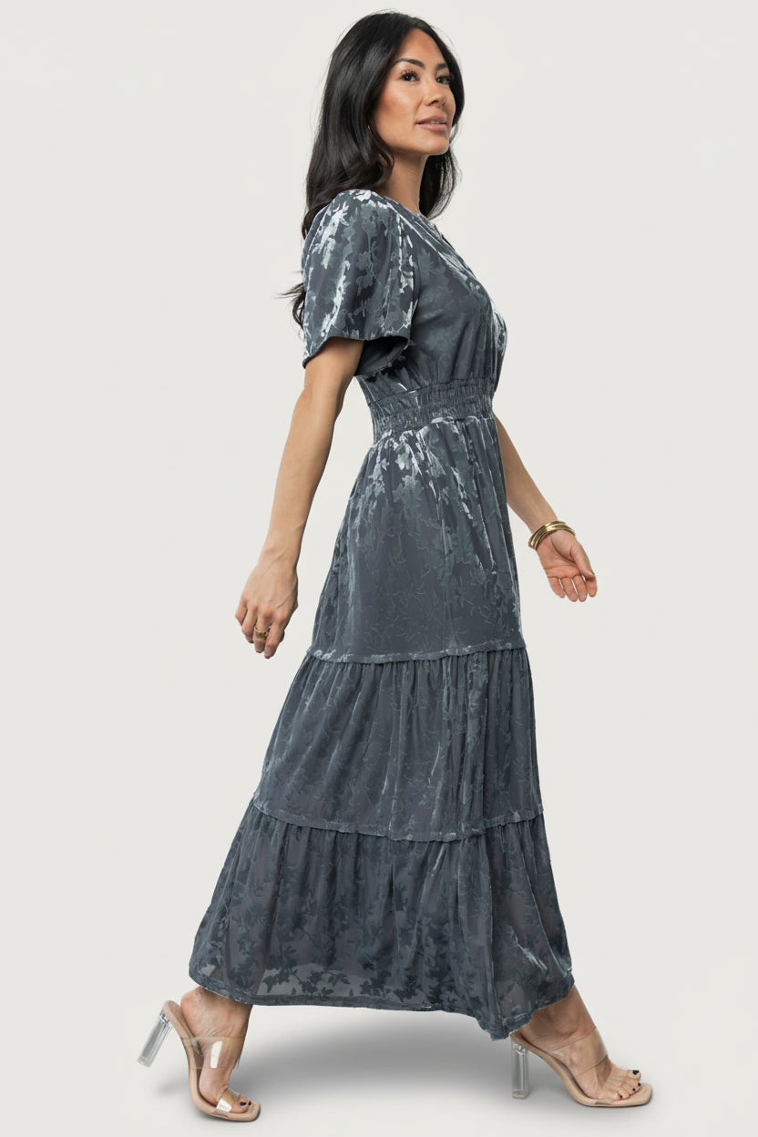Model styling the Bronwyn Velvet Dress in Dusty Blue with accessories, showing versatile look for weddings, parties, and holiday events.