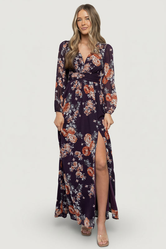 Full-length front view of model wearing Adira plum floral maxi dress with V-neck, smocked back, bishop sleeves, and left leg slit, showing drape.