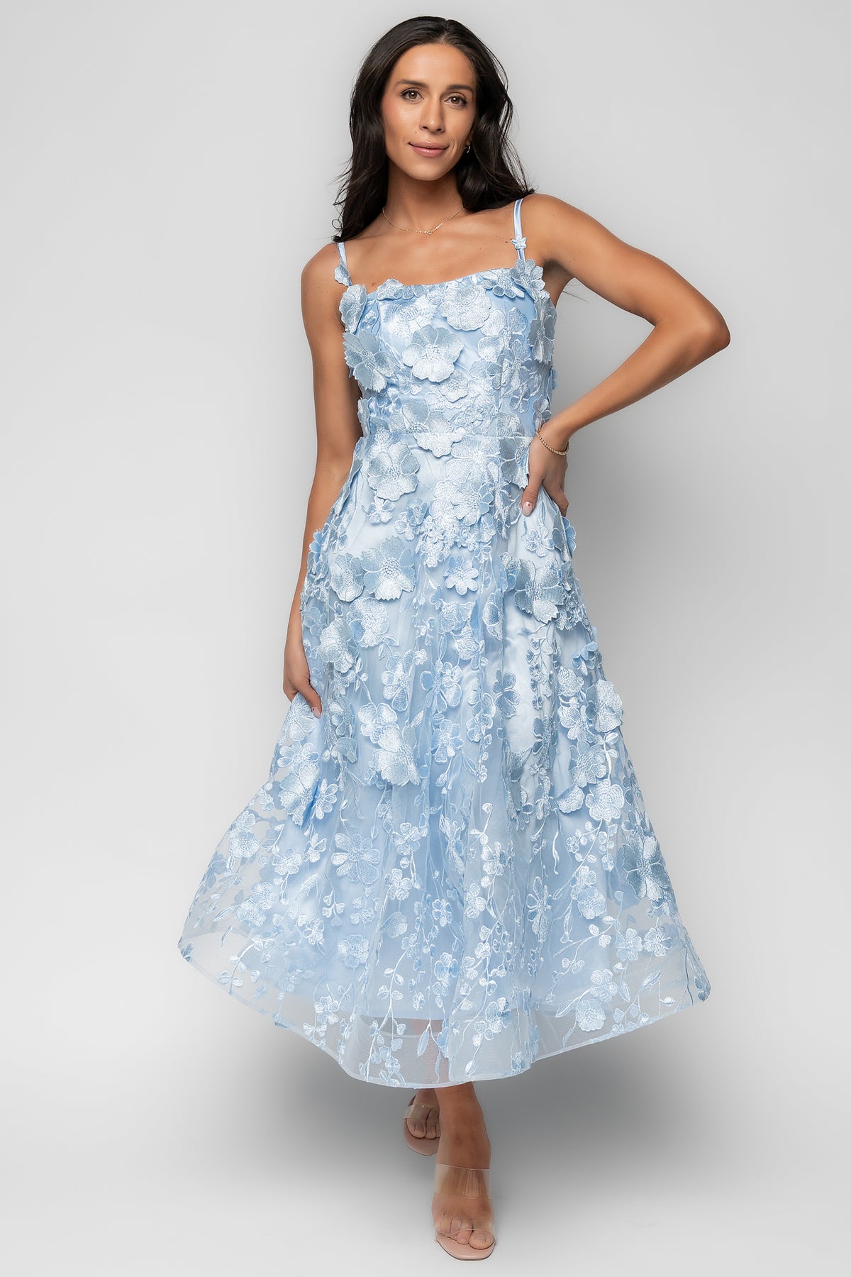Front view of light blue midi dress on model showing square neckline, adjustable straps, and delicate floral appliqué over mesh.