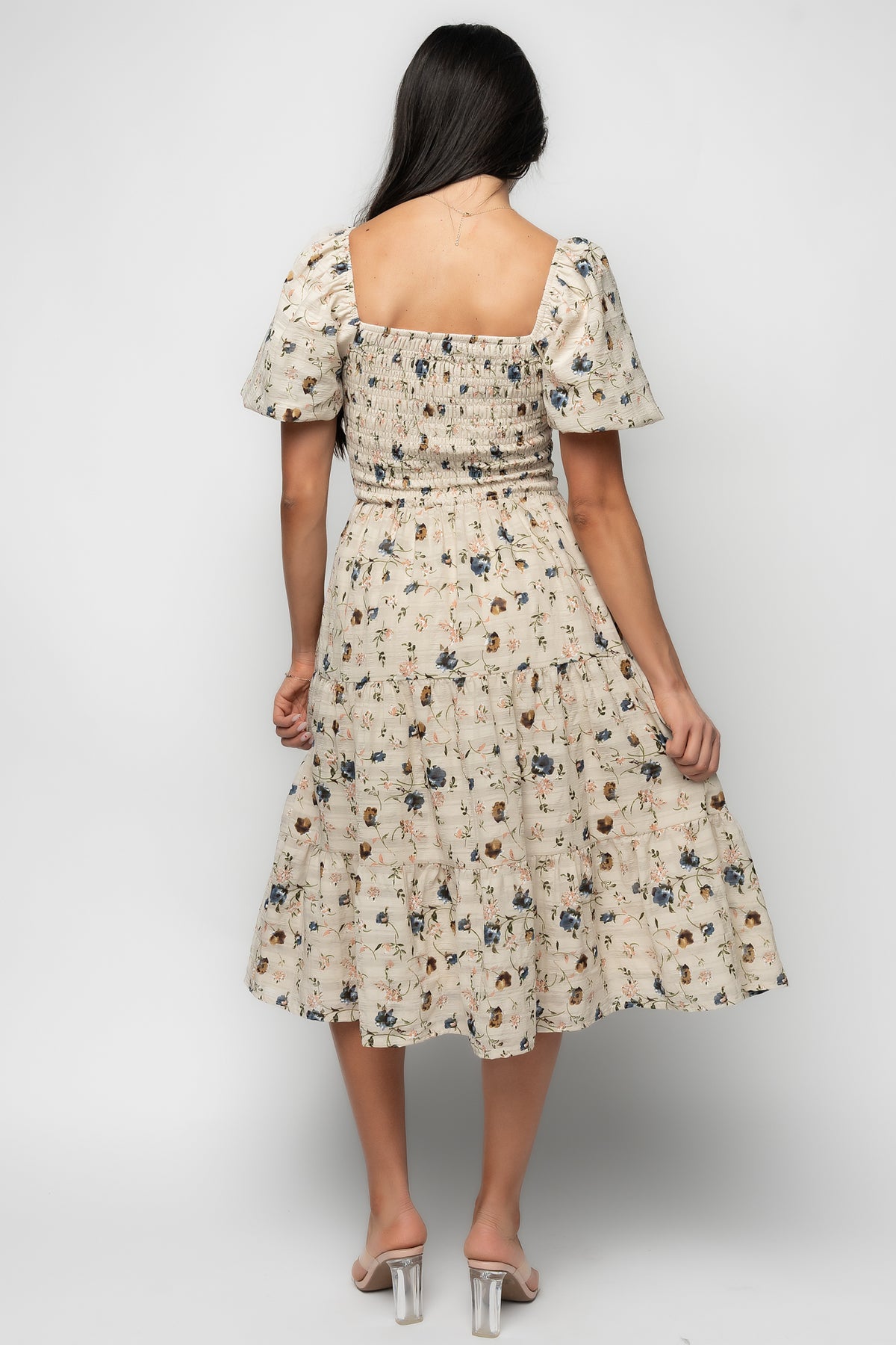 Three-quarter view of Mattea smocked midi dress in beige floral, showing tiered skirt movement and overall silhouette on model.