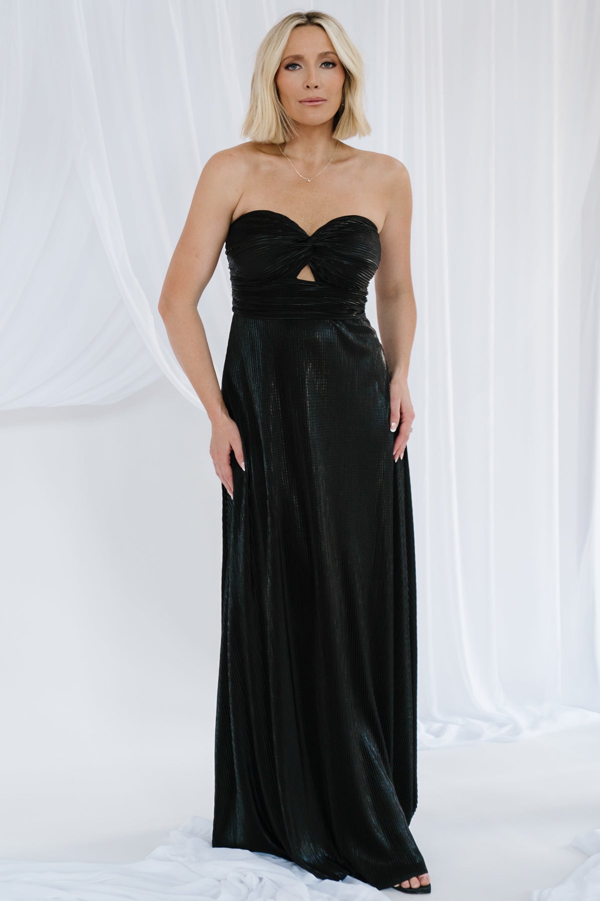 Model in full-length Seraphine strapless metallic pleated maxi gown in black, showing flowing skirt and evening silhouette.