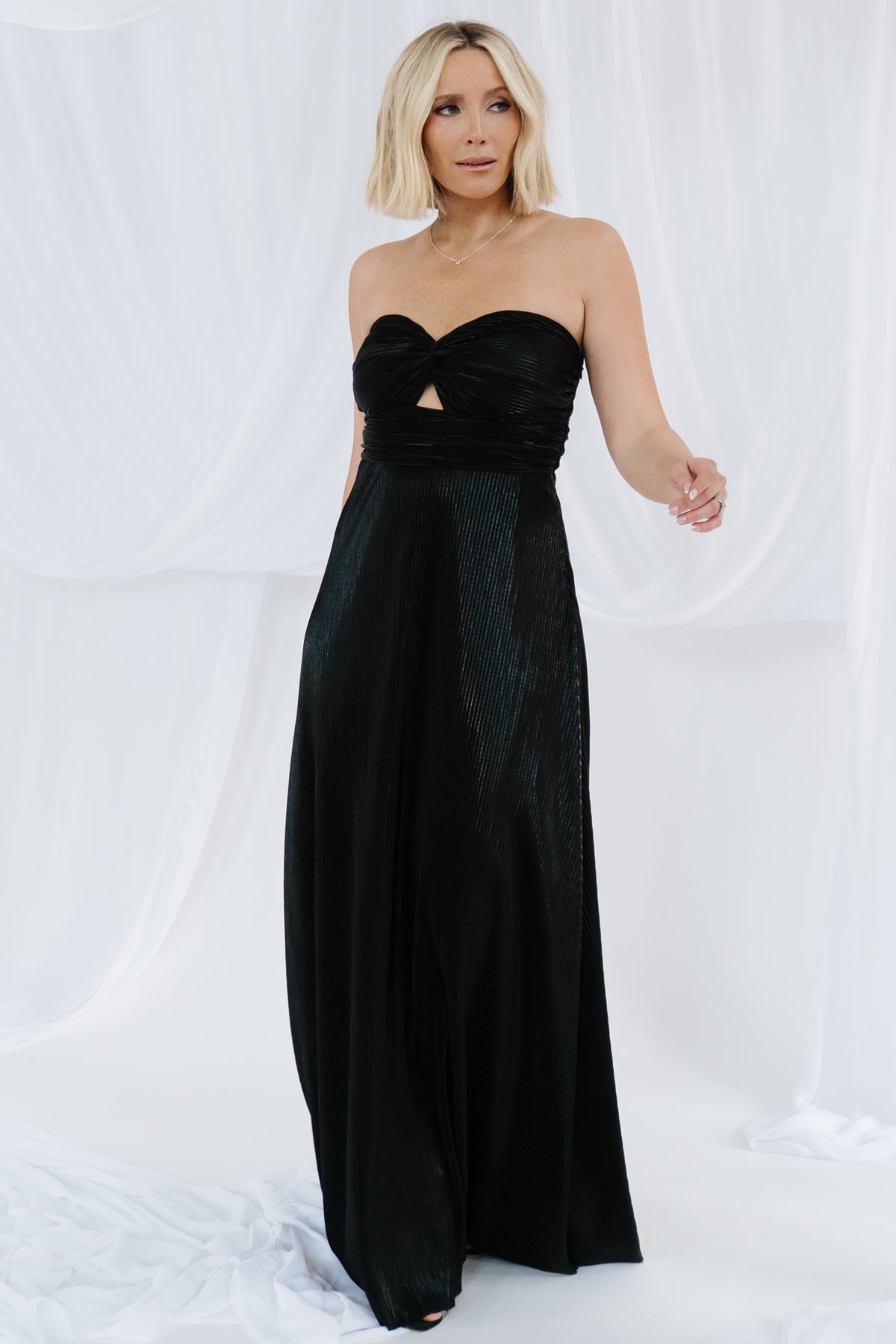 Back and hip view of the black metallic pleated gown showing lined skirt, smooth finish and flattering maxi length.
