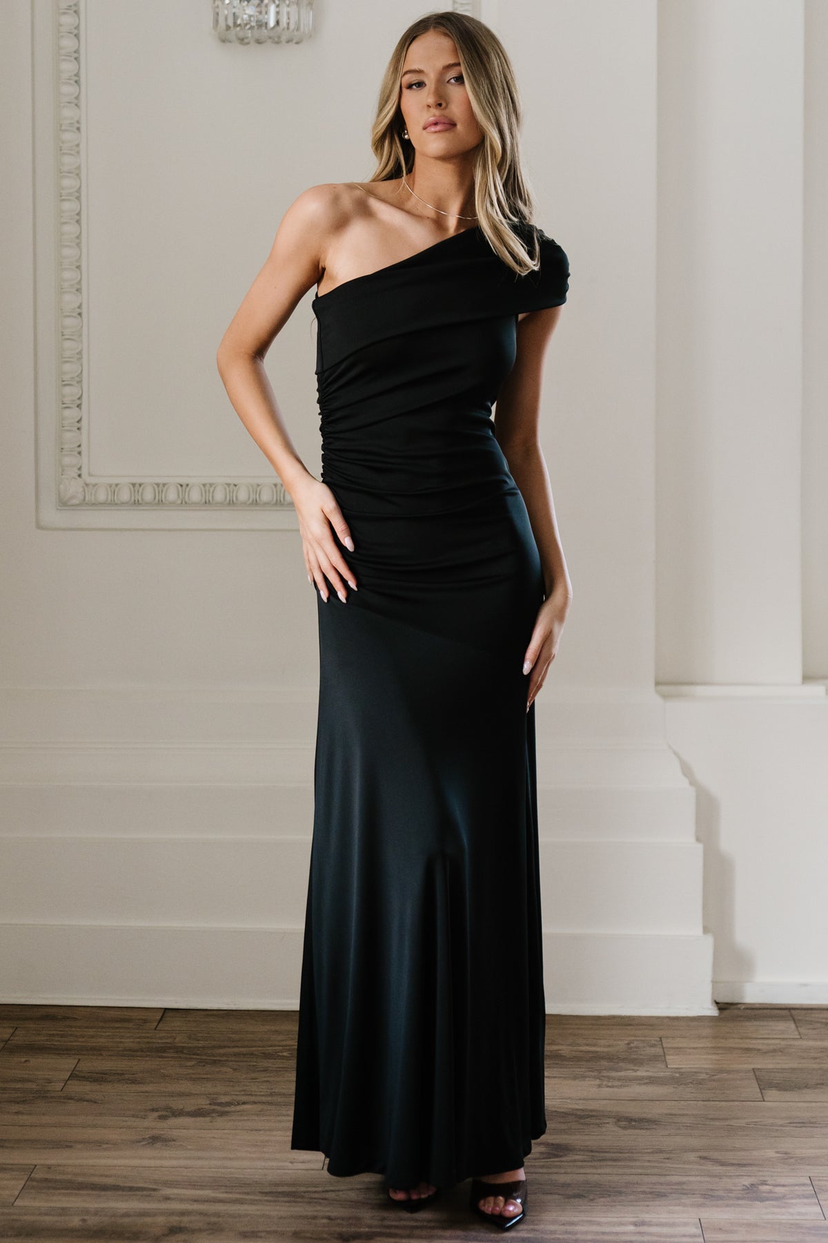 Front view of Leon one-shoulder black maxi gown on model showing asymmetrical neckline, diagonal bodice draping, and right-side ruching.