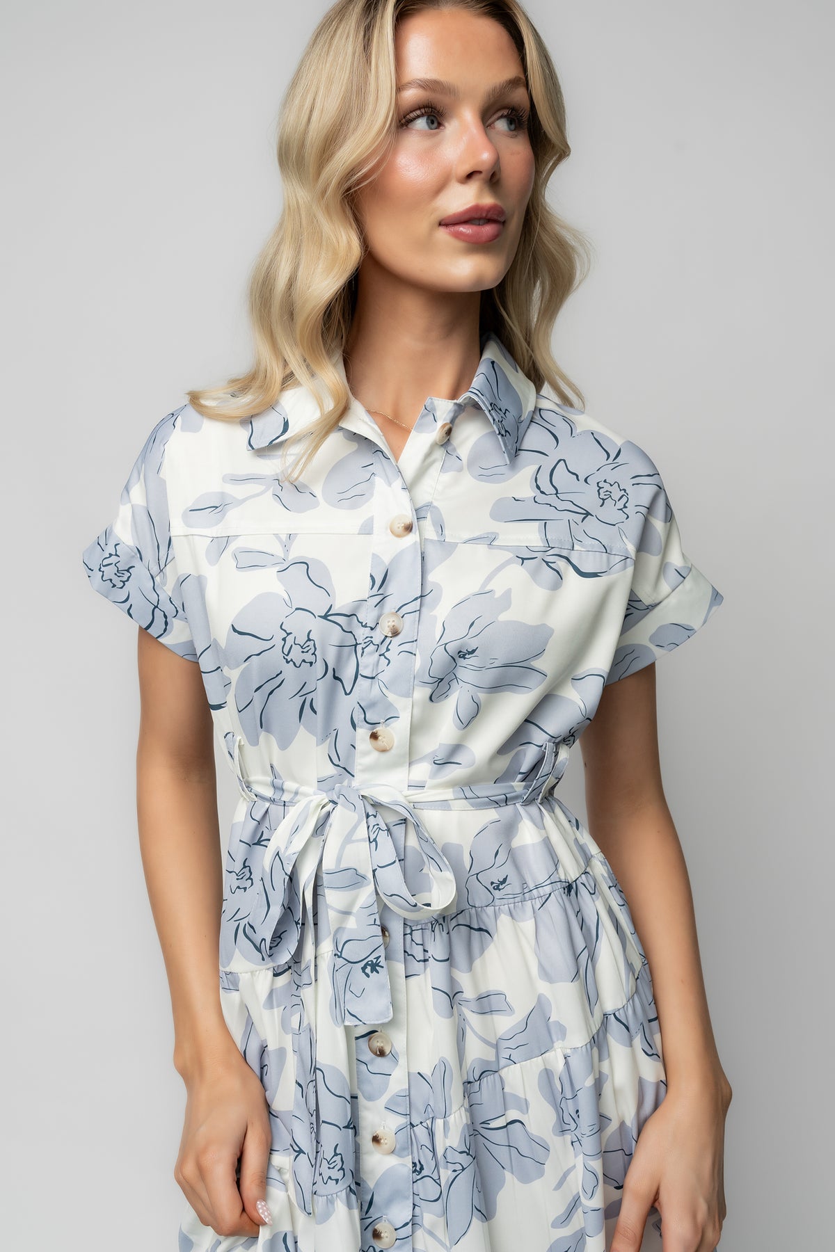 Model walking in Claire Button Up Midi Dress featuring tiered hem movement and ivory fabric patterned with blue florals.