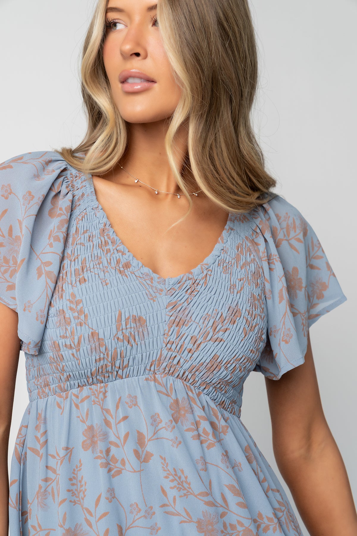 Close-up of smocked center-seamed bodice and upturned V high waist showing elastic smocking and fabric texture in dusty blue.