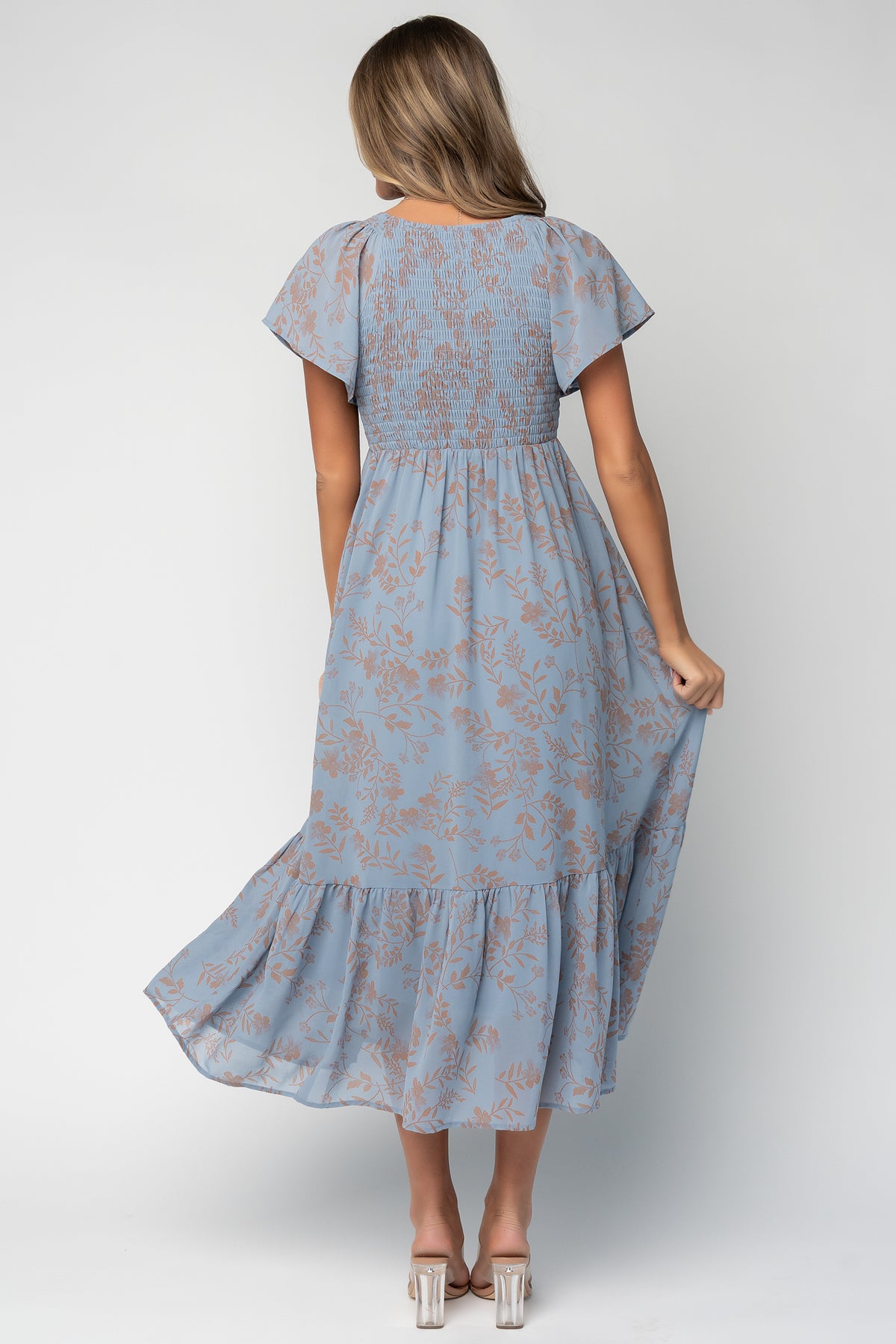 Back and movement shot of the dusty blue dress showing skirt drape, single bottom tier, and subtle sheen of the fabric.