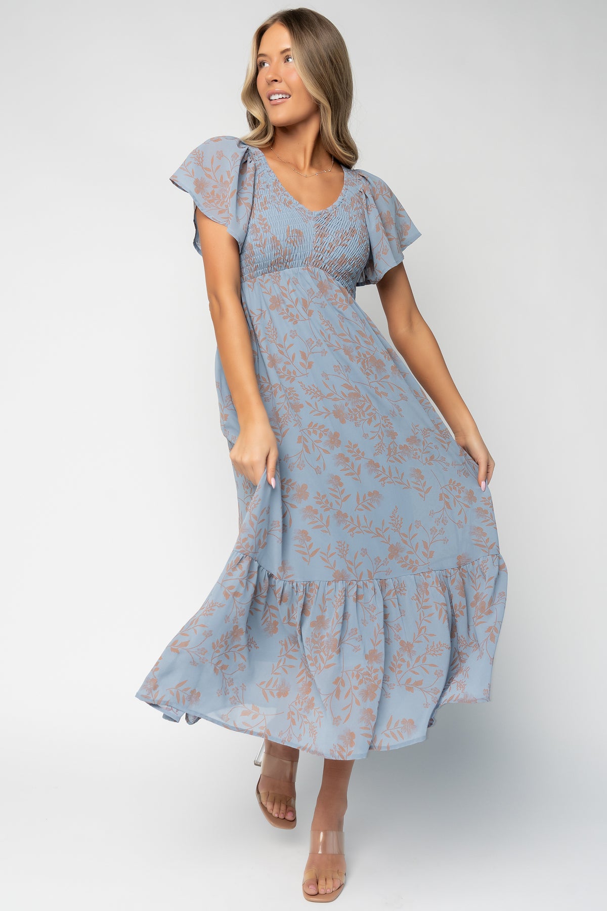 Front view of Monica Smocked Maxi Dress in dusty blue with terracotta floral print, V-neckline and flutter sleeves, full-length view.