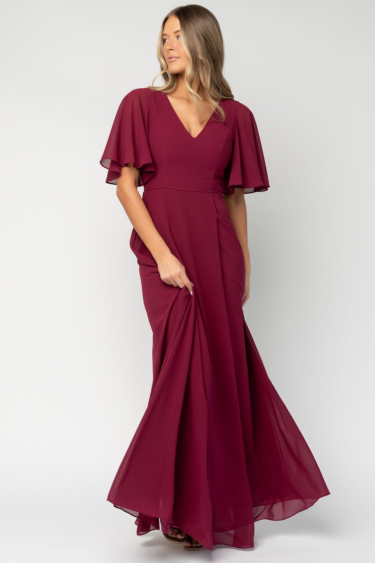 Front view of model wearing wine Valetta Maxi Dress showing V-neck, flutter sleeves and flowing chiffon skirt with left leg slit.