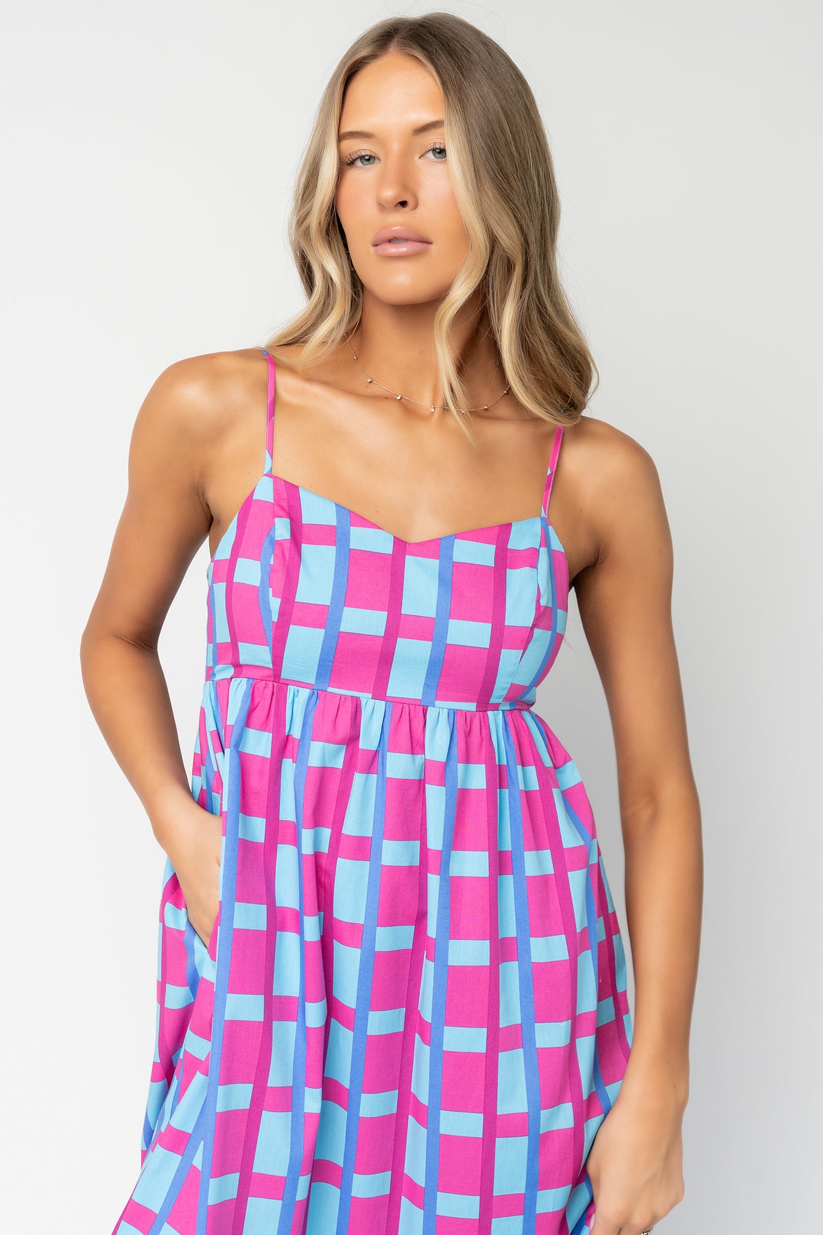 Close-up of pink-and-blue geometric check print and cotton texture; shows stitchwork and lining that reaches mid-thigh.