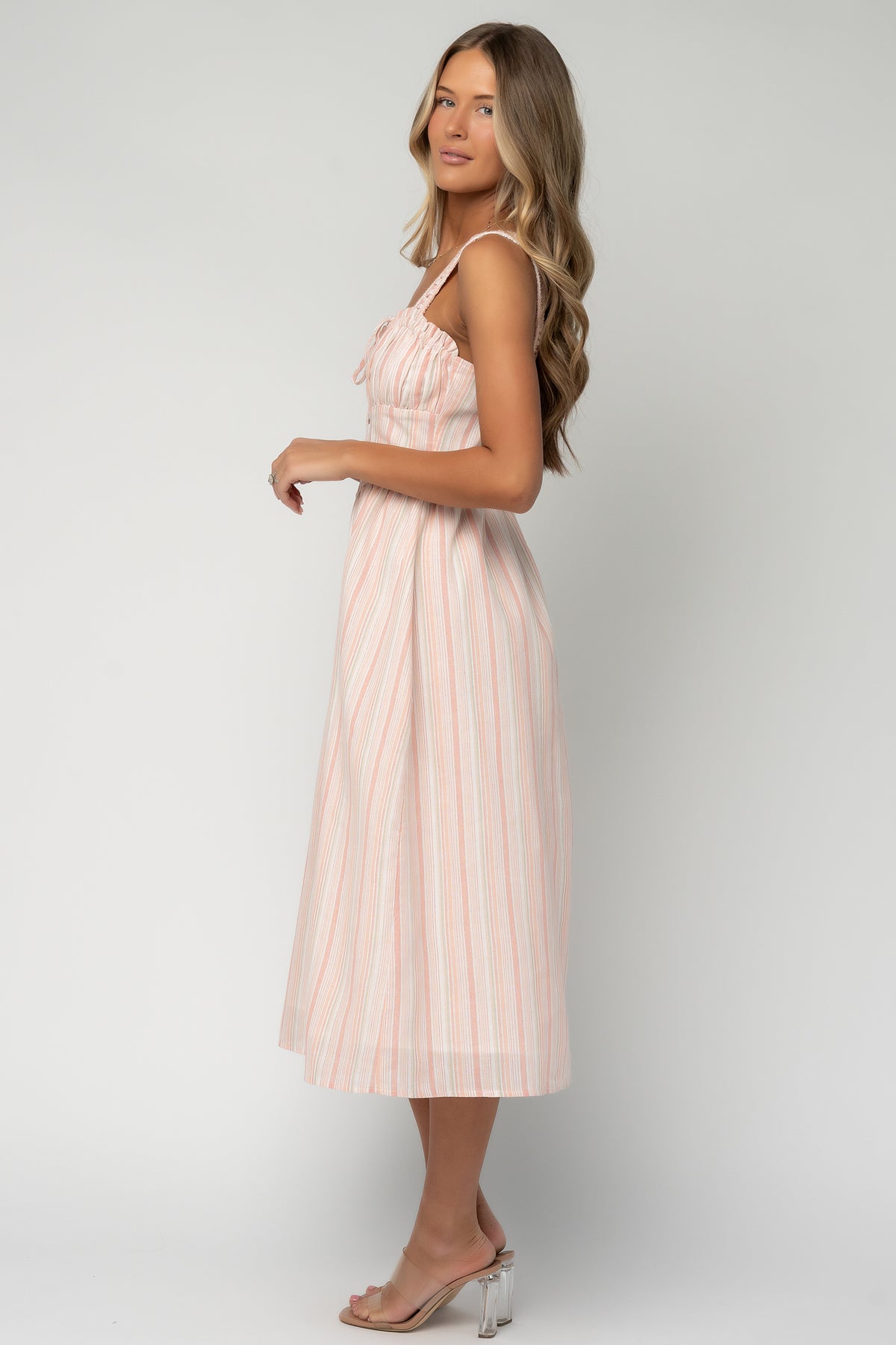 Back view of Melina Midi Dress displaying the hidden back zipper, fitted bodice silhouette and the peach, green and ivory vertical stripe pattern at midi length.