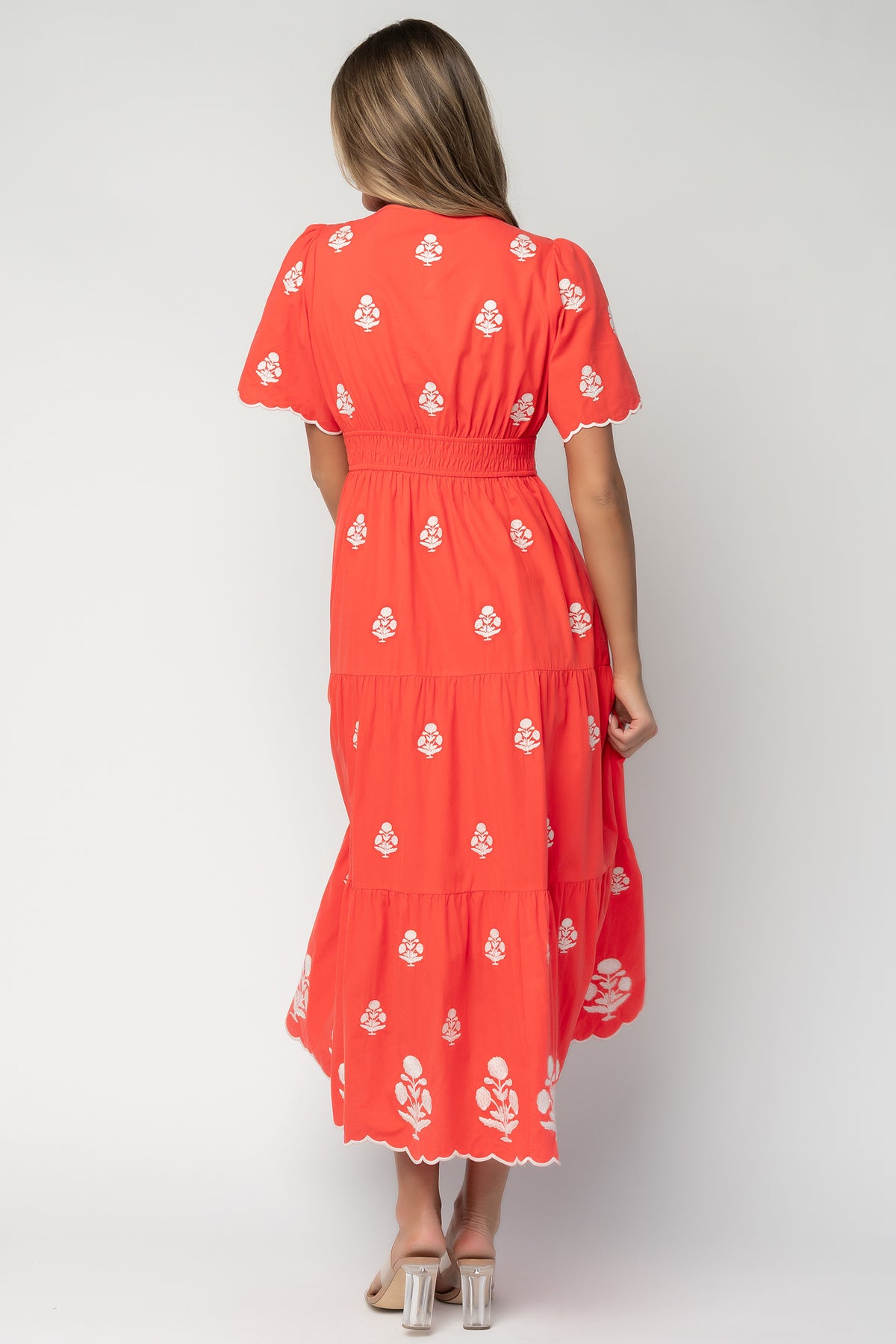Side view of Delilah embroidered maxi dress showing smocked elastic waistband, pocket opening, and flowing tiered silhouette in red.