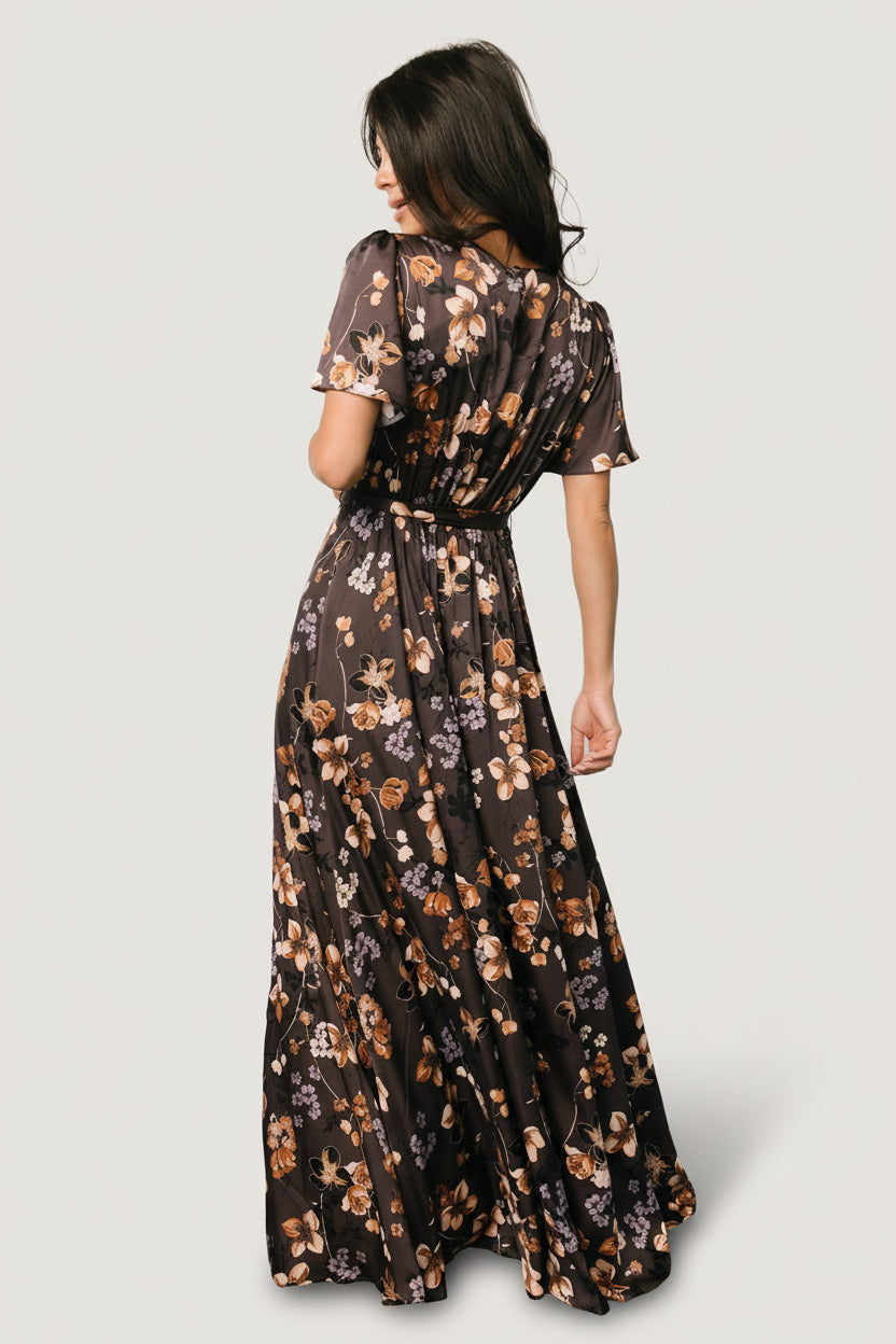 Side view of brown floral satin maxi dress on model showing natural waist with removable tie and the left leg slit in motion.