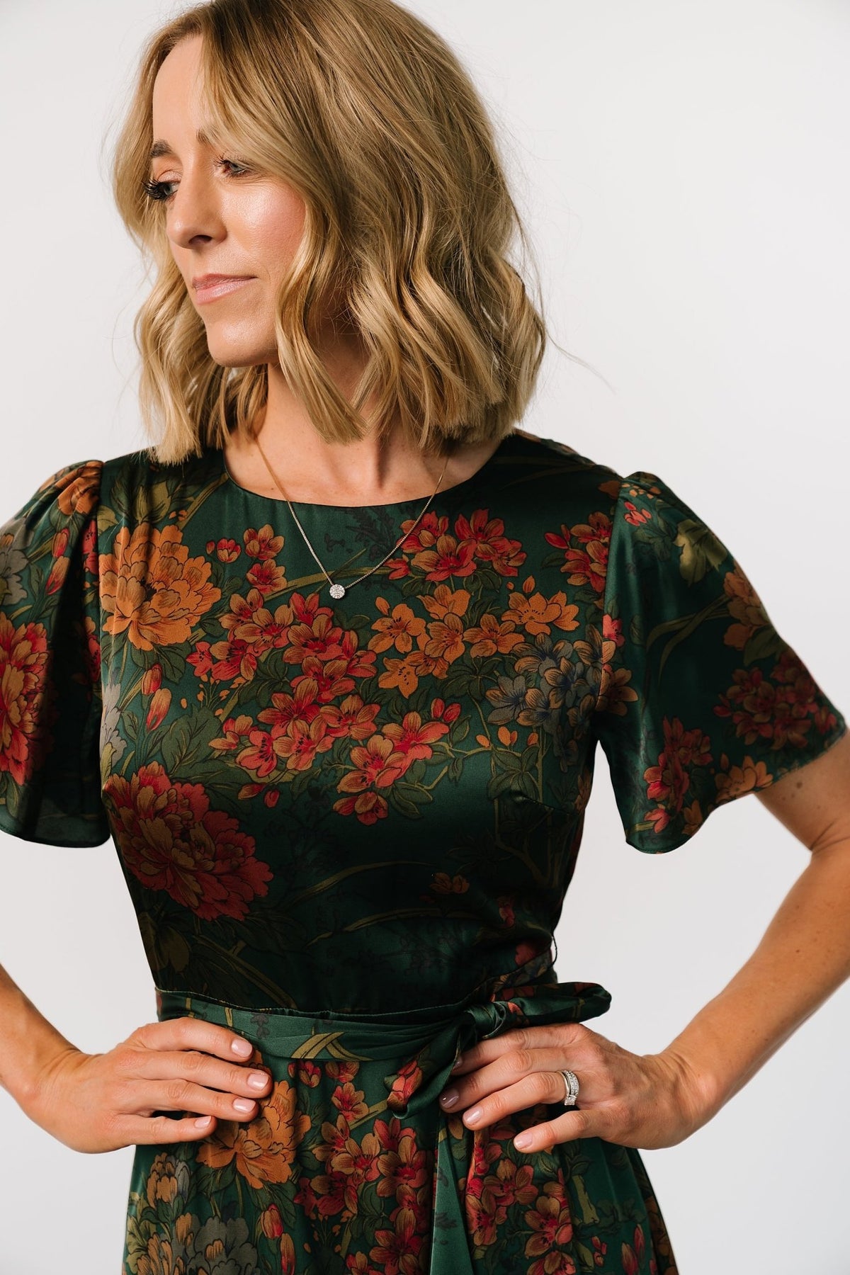 Full-length studio shot of dark green floral satin maxi dress on model, showing silhouette, sleeve length, and skirt sweep.