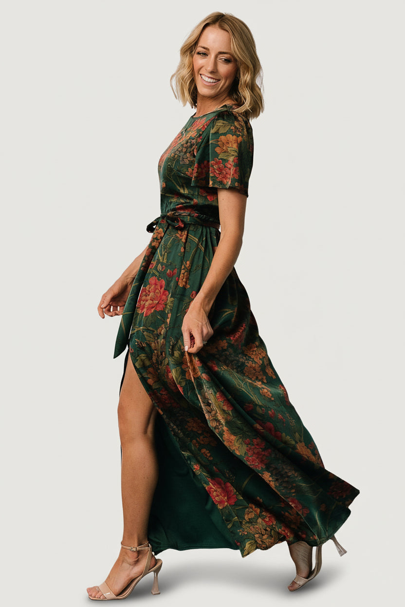 Side-angle shot of dark green floral satin maxi dress highlighting flutter sleeve, rounded neckline, and flowing hemline.