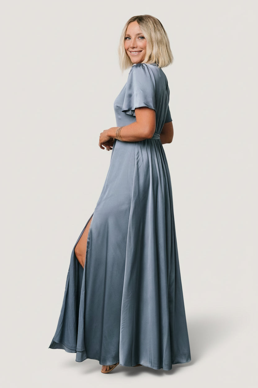 Side view of whisper blue satin maxi dress emphasizing the left leg slit, natural waist with removable tie, and fluid movement of the skirt.