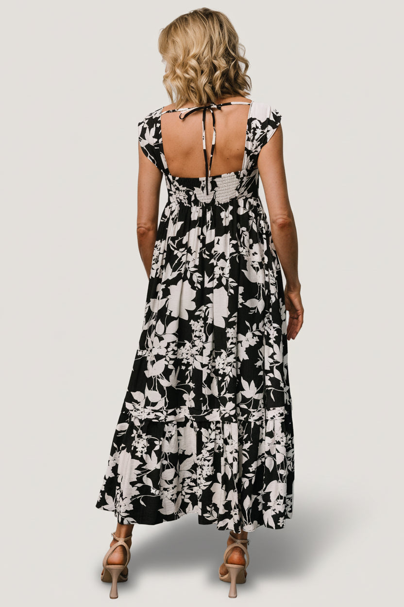 Close-up of dress bodice showing square neckline, smocked back detail and gathered cap sleeve construction in black and ivory floral print.