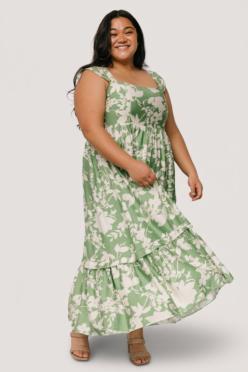 Green and ivory floral maxi dress worn by model, square neckline, smocked back, gathered tank cap sleeves, and functional side pockets on display.