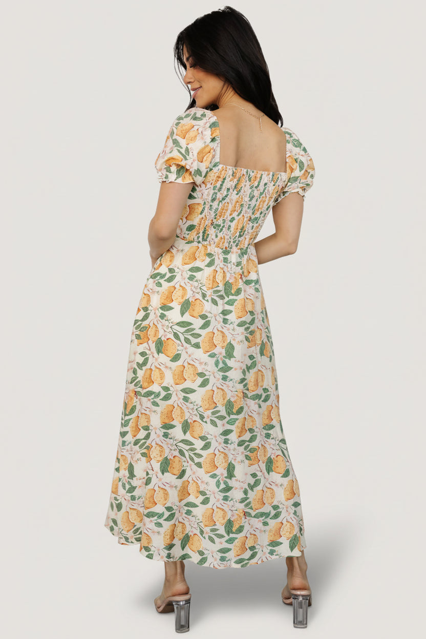 Back view of Amalfi midi dress showing smocked back, gathered waistline, elastic sleeve cuffs, and the lemon-print pattern across the skirt.