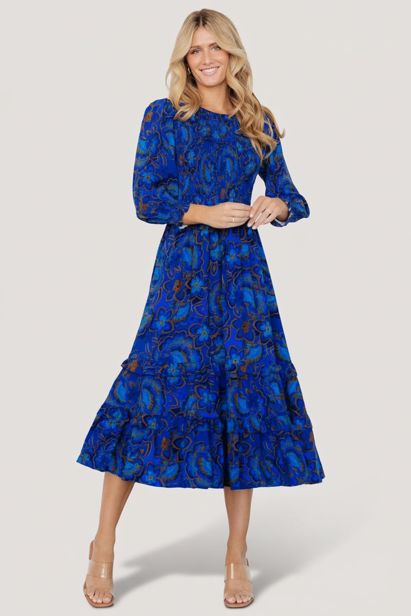 Front view of cobalt-blue midi dress with vibrant multicolor florals, smocked bodice, elastic waist, and tiered ruffle skirt.