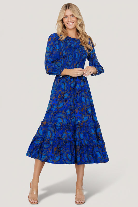 Front view of cobalt-blue midi dress with vibrant multicolor florals, smocked bodice, elastic waist, and tiered ruffle skirt.
