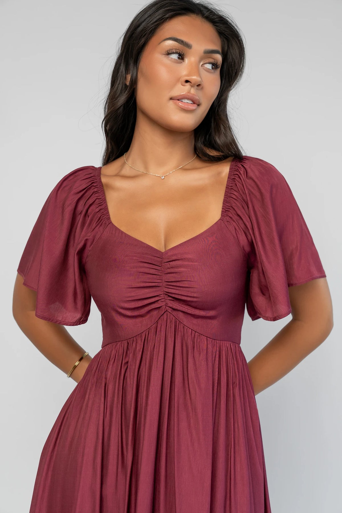 Anisa Midi Dress in Burgundy with a wide V-neckline, cinched bust, elastic shoulders, and a tiered skirt.