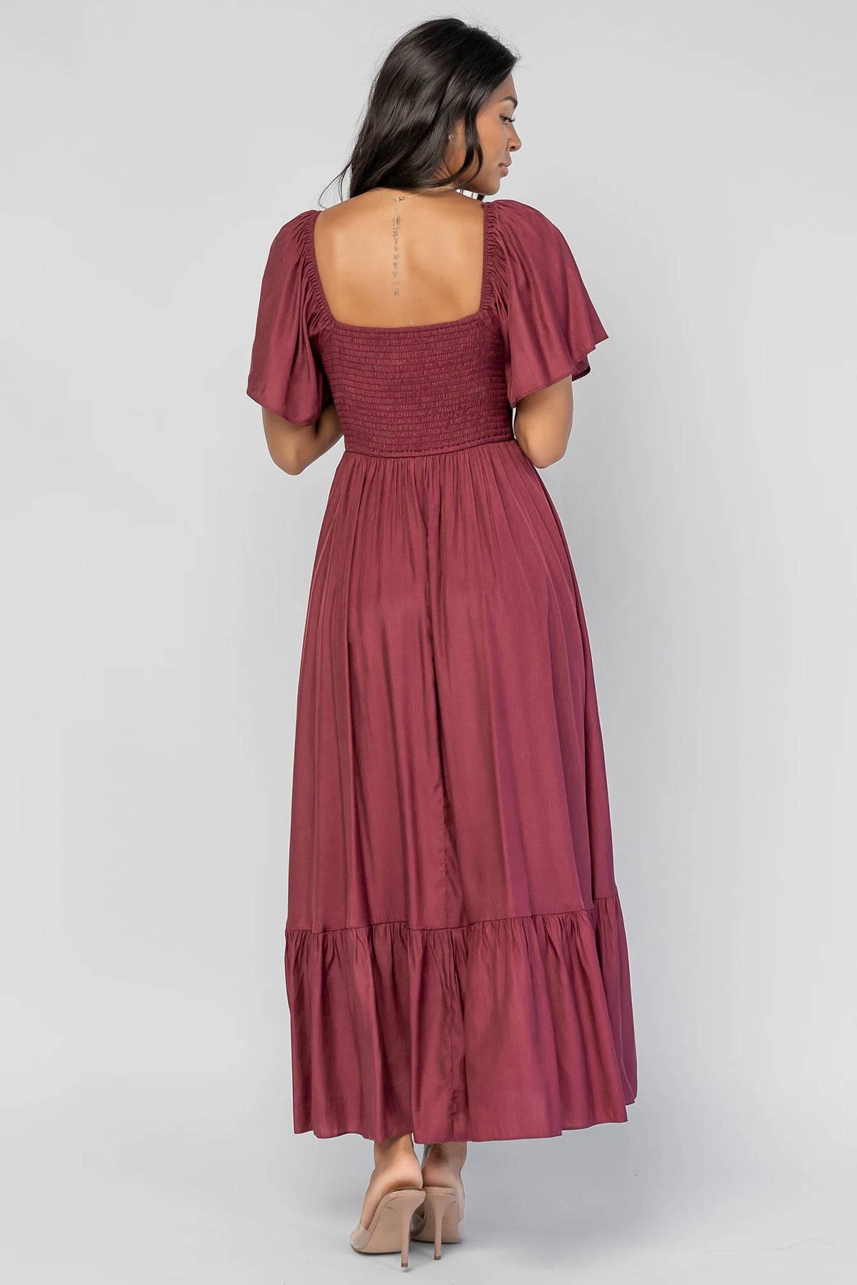 Anisa Midi Dress in Burgundy with a wide V-neckline, cinched bust, elastic shoulders, and a tiered skirt.