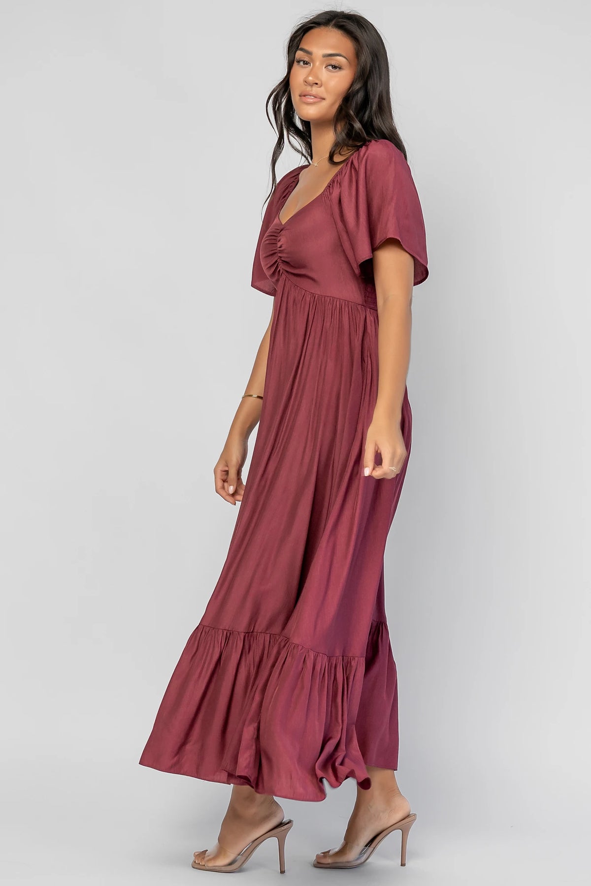 Anisa Midi Dress in Burgundy with a wide V-neckline, cinched bust, elastic shoulders, and a tiered skirt.