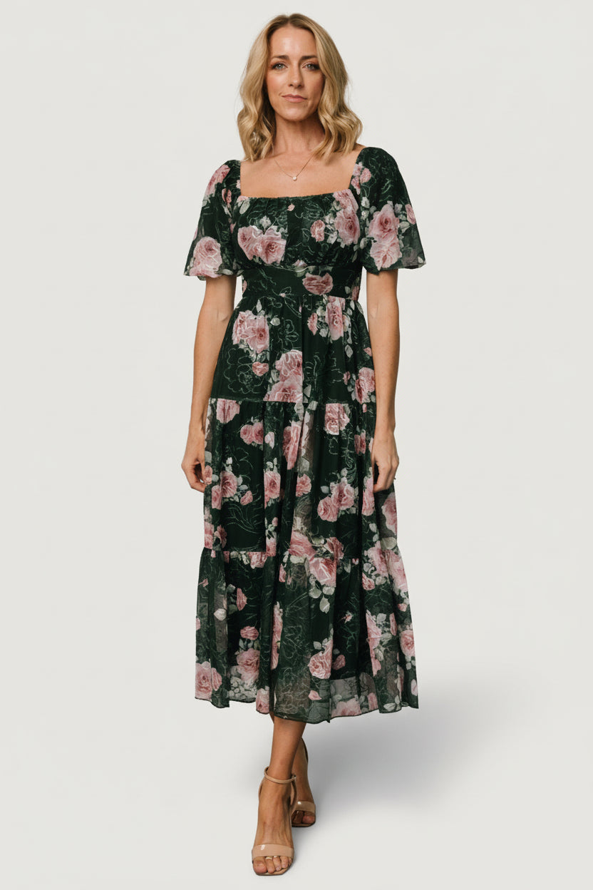 Front view of model wearing dark green embroidered tulle midi dress with pink floral accents, smocked back and three-tier skirt (full length).