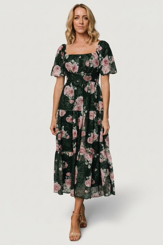 Front view of model wearing dark green embroidered tulle midi dress with pink floral accents, smocked back and three-tier skirt (full length).