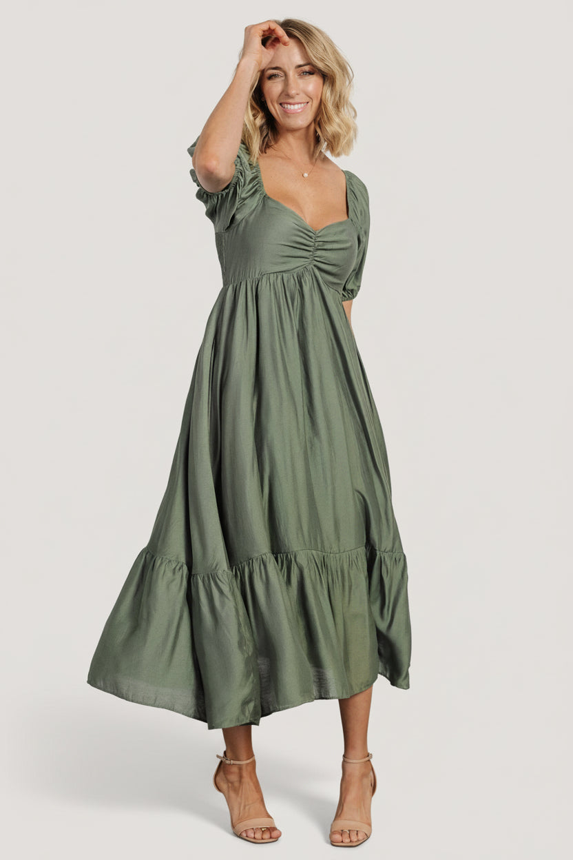 Lifestyle photo of the Annalisa midi dress in dusty olive on location, demonstrating movement, length, and occasion-ready styling.