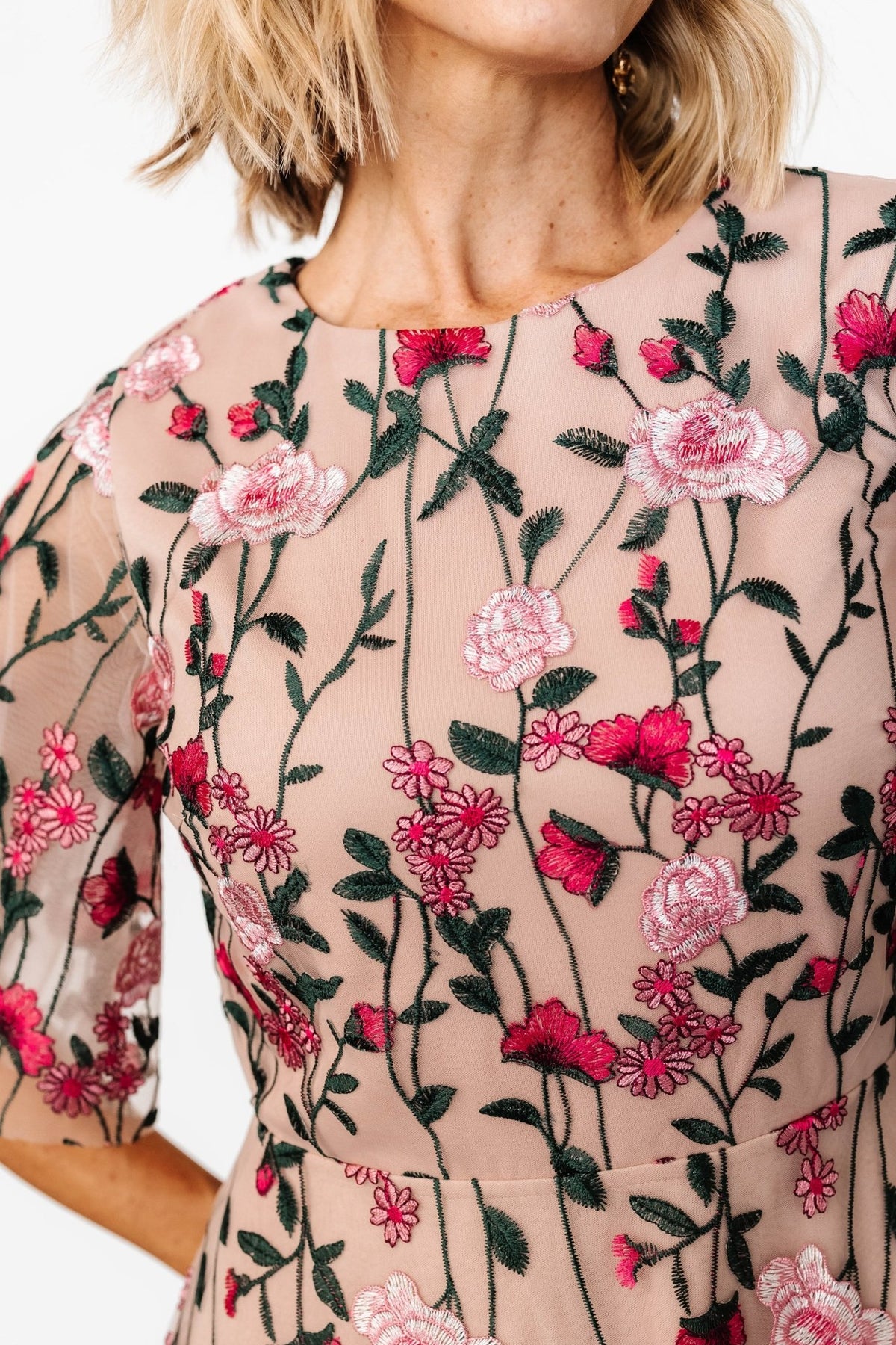 Close-up of embroidered bodice showing detailed pink, green and off‑white floral stitching on sheer tulle overlay and lined interior.